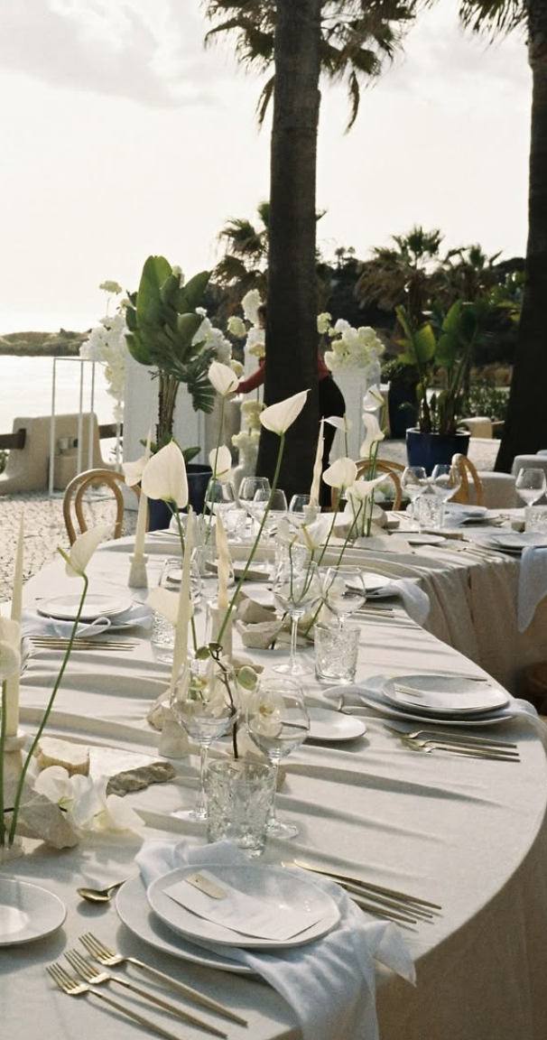 Outdoor wedding dinner tables with white flowers and palm trees by the sea